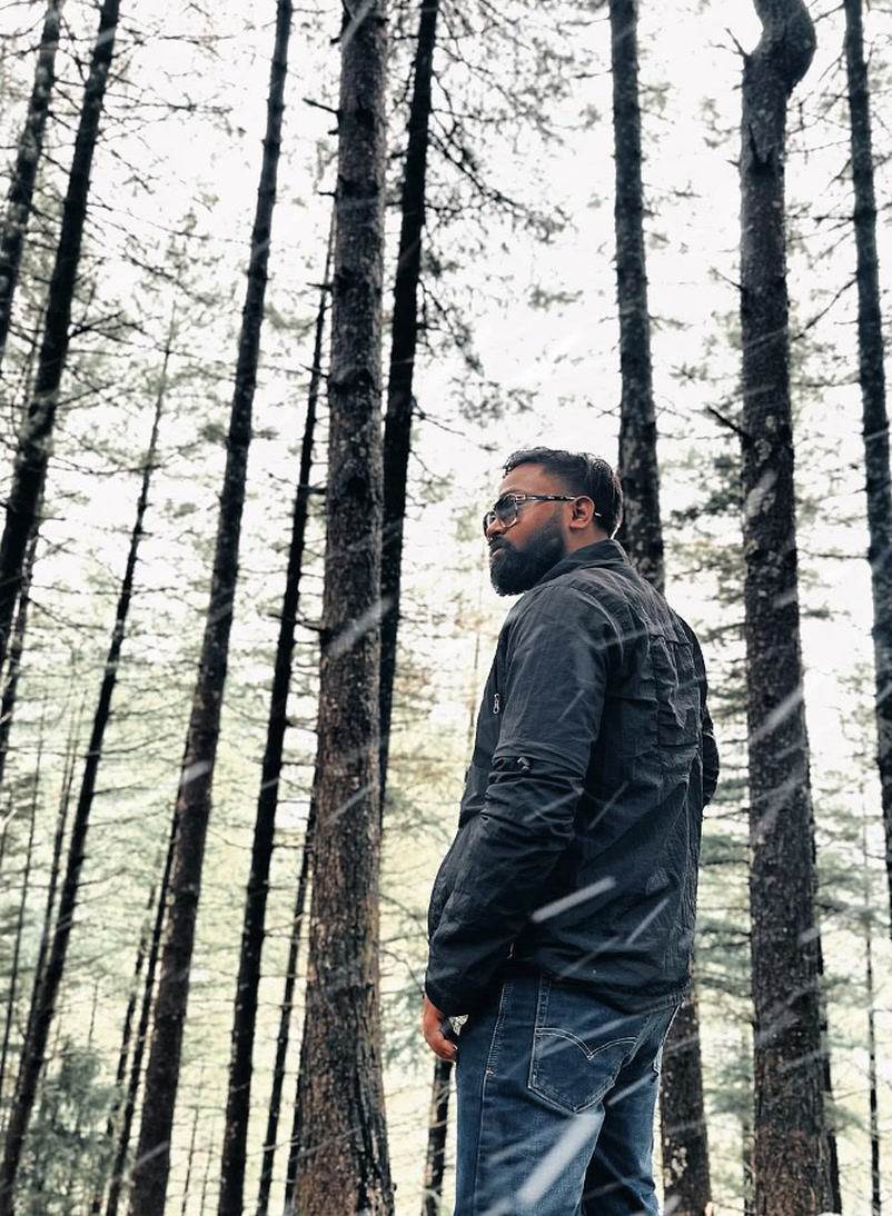 Devansh Kushwah standing in misty pine forest in light snowfall pre-wedding location scouting — Directed by Devansh Kushwah